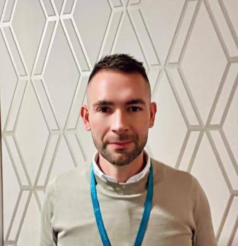 man with brown hair wearing a beige jumper smiling having his photo taken for the team page
