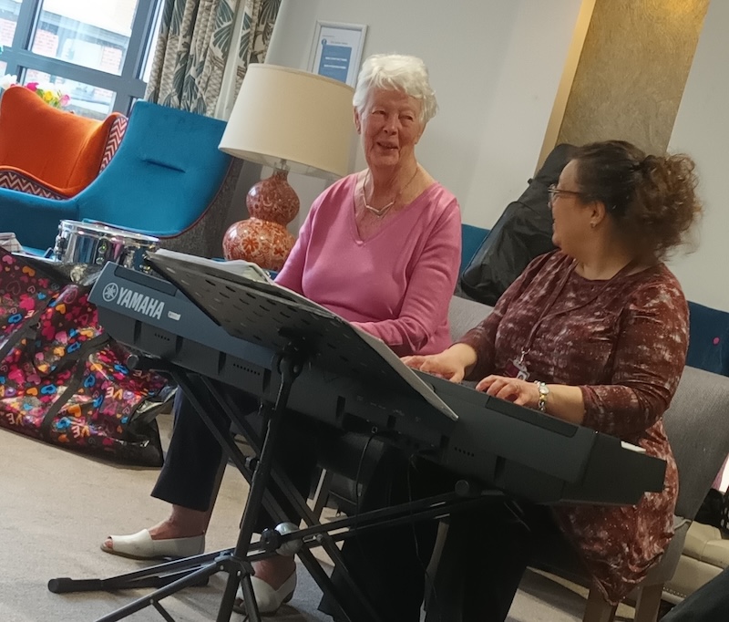 resident having a 1-1 music therapy session with a local visiting musician playing the piano and singing