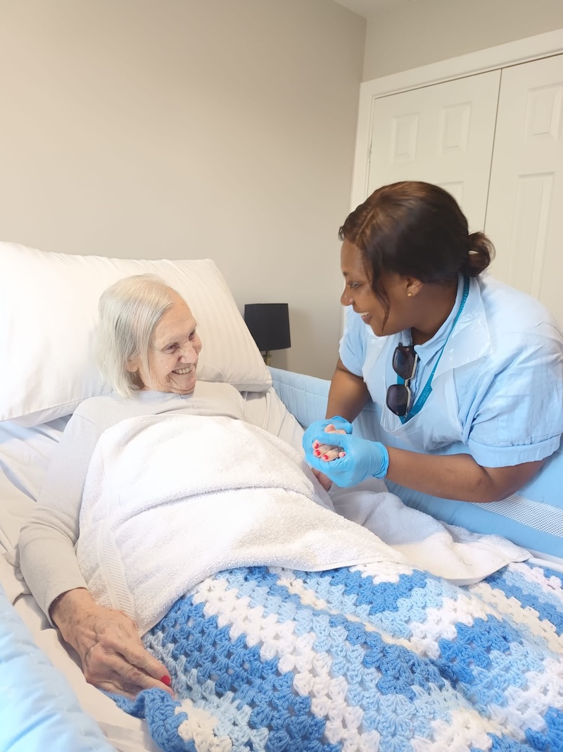 carer holding hands with a resident who is laying in a bed