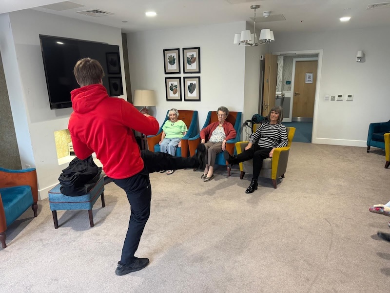 a group of residents sat down in armchairs doing exercise with a team member