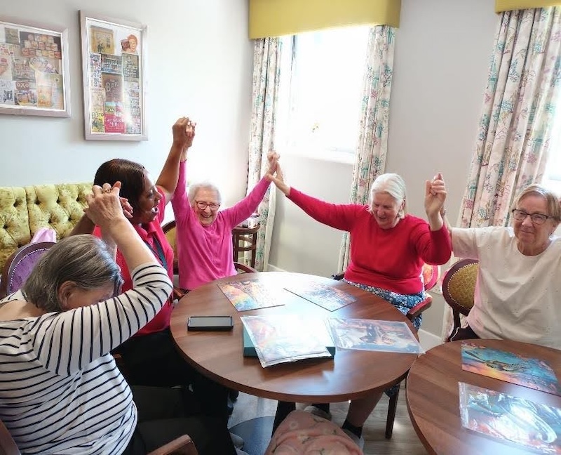 a group of residents sat around a table smiling and holding hands